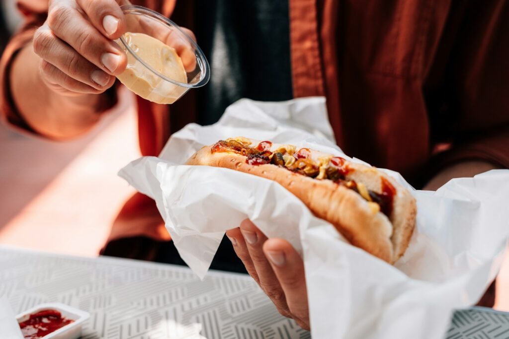 a person adding a topping to a hot dog