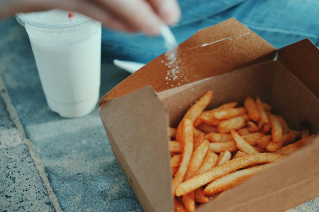 person sprinkling salt on fresh french fries